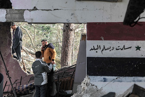 أشخاص يتفقدون الدمار في موقع مستودع أسلحة تعرض للقصف الإسرائيلي في ريف طرطوس (أ ف ب)
