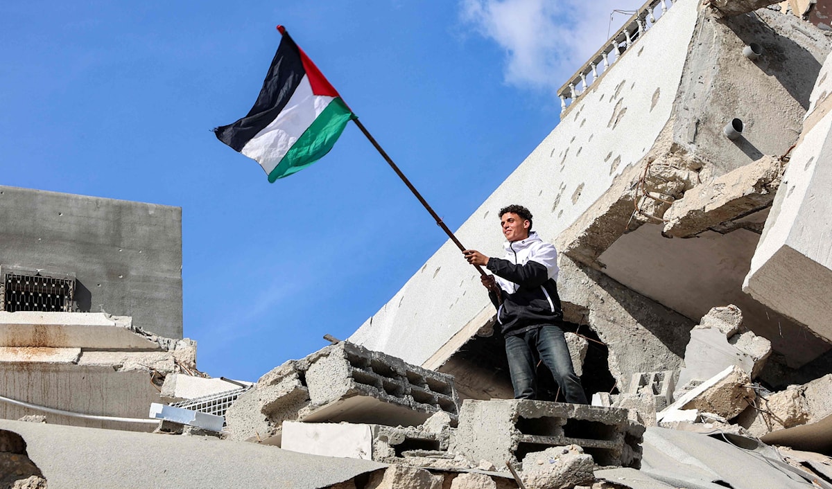 رجل يرفع العلم الفلسطيني فوق أنقاض مبنى منهار في مخيم جباليا شمال قطاع غزة (أ ف ب)