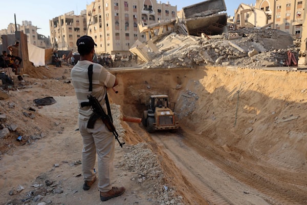 مقاتل فلسطيني يراقب جرافة تحفر بحثاً عن جثامين أسرى إسرائيليين في خانيونس (أ ف ب)