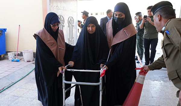 عجوز عراقية تتلقى مساعدة للوصول إلى صندوق الاقتراع في النجف للإدلاء بصوتها (أ ف ب)