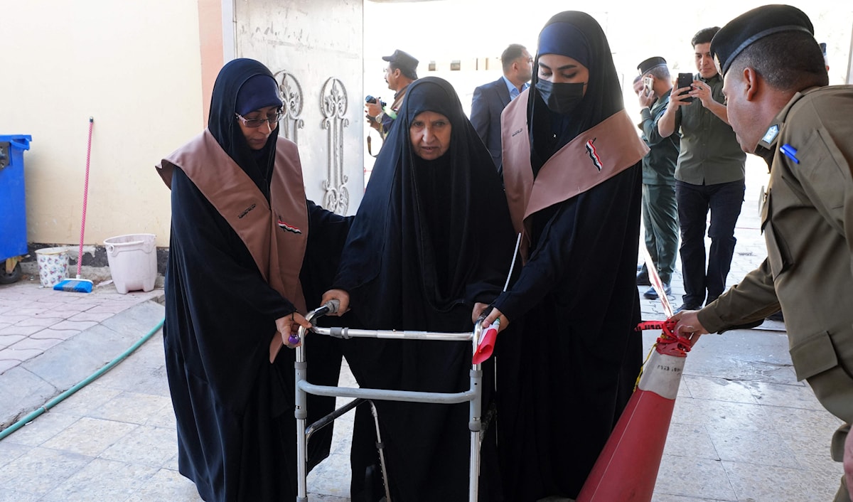 عجوز عراقية تتلقى مساعدة للوصول إلى صندوق الاقتراع في النجف للإدلاء بصوتها (أ ف ب)