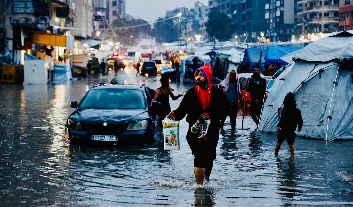 نازحون يسيرون عبر مياه الفيضانات عقب هطول أمطار غزيرة في مدينة غزة (أ ف ب)