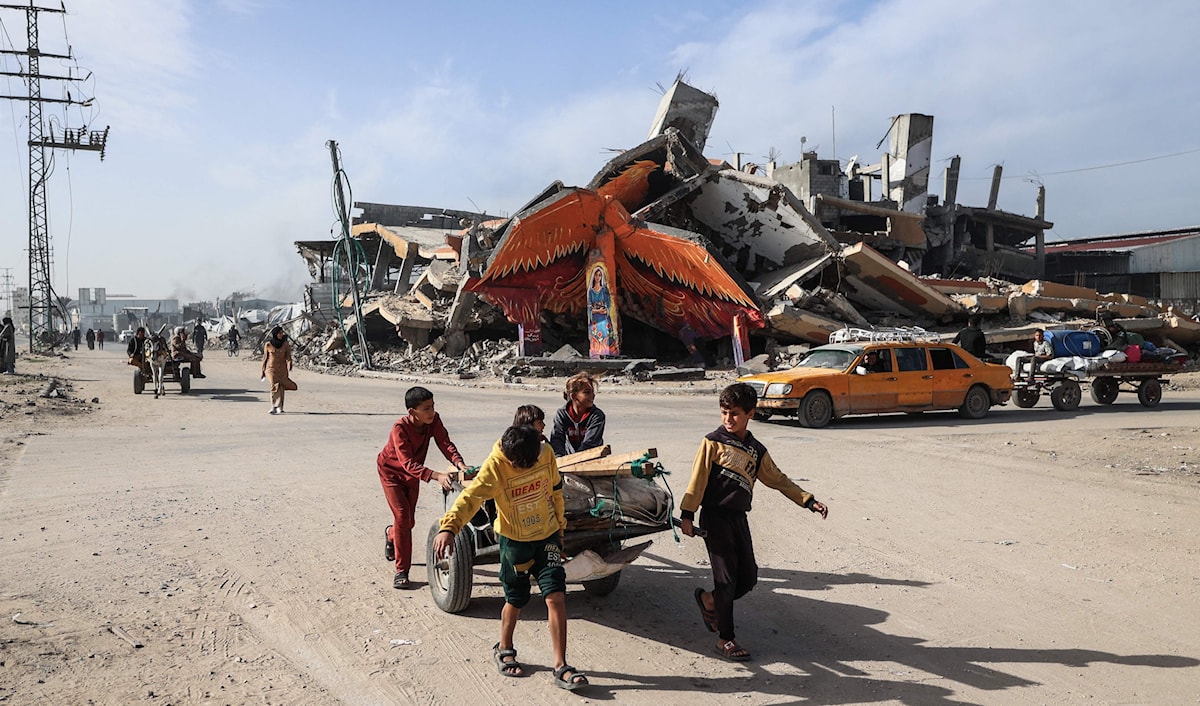 أطفال يجرون عربة أمام جدارية على مبنى مدمر في مخيم المغازي للاجئين قرب دير البلح (أ ف ب)