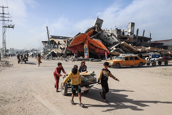 أطفال يجرون عربة أمام جدارية على مبنى مدمر في مخيم المغازي للاجئين قرب دير البلح (أ ف ب)
