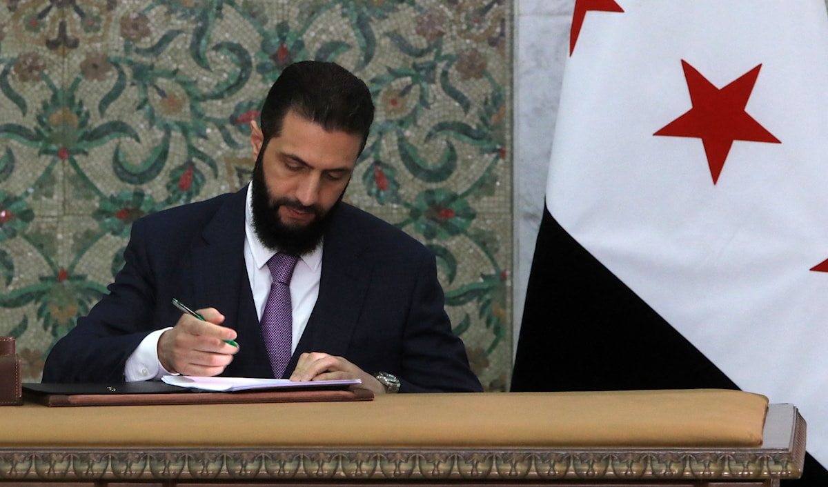 الرئيس السوري الانتقالي أحمد الشرع وهو يوقع مسودة الإعلان الدستوري (أ ف ب)