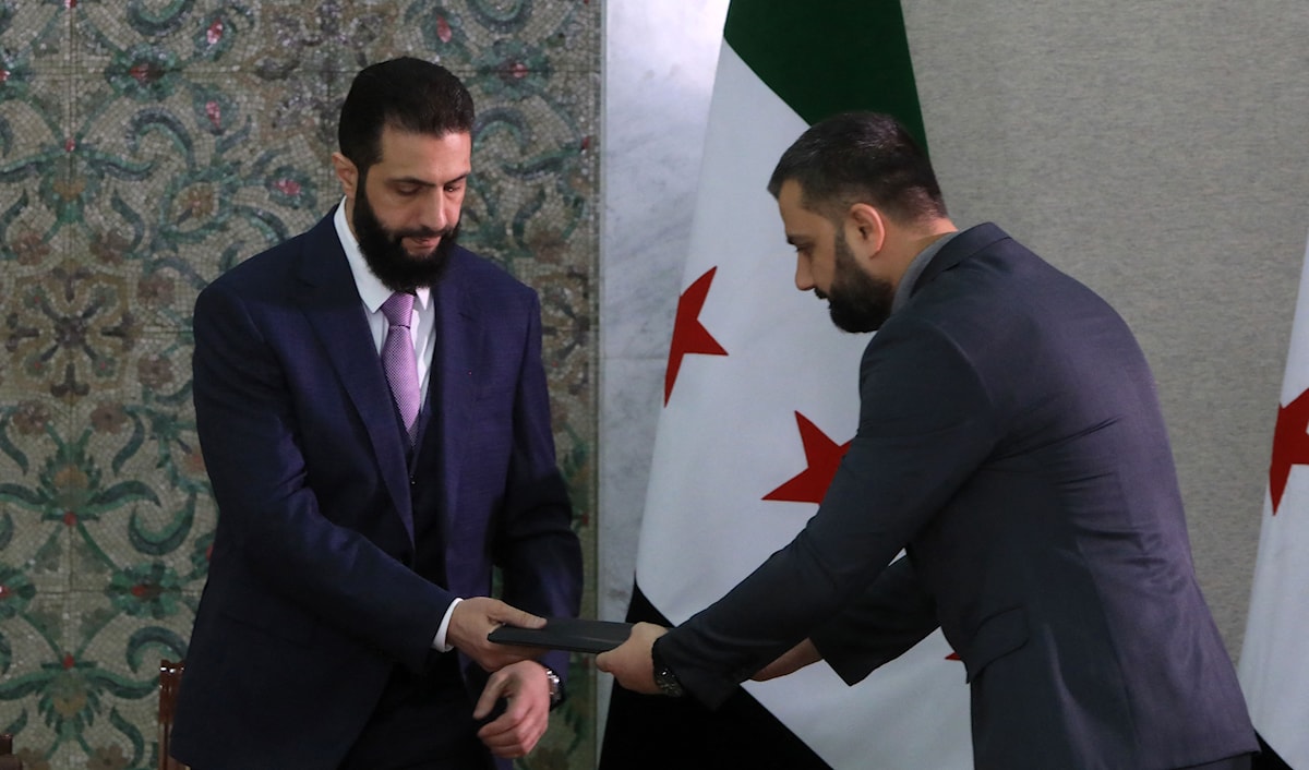 الرئيس السوري الانتقالي أحمد الشرع خلال توقيعه الإعلان الدستوري (أ ف ب)