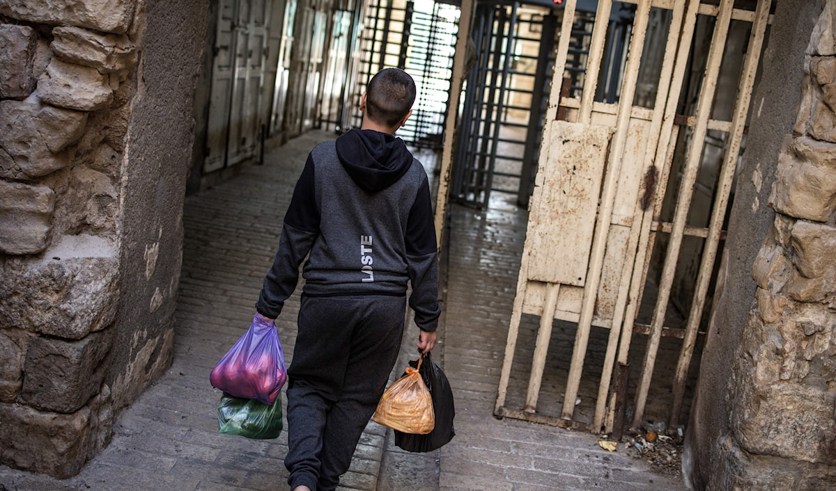 فتى فلسطيني يحمل أكياس أغذية بينما يتوجه نحو عائق وضعه الاحتلال في المدينة القديمة في الخليل (أ ف ب)