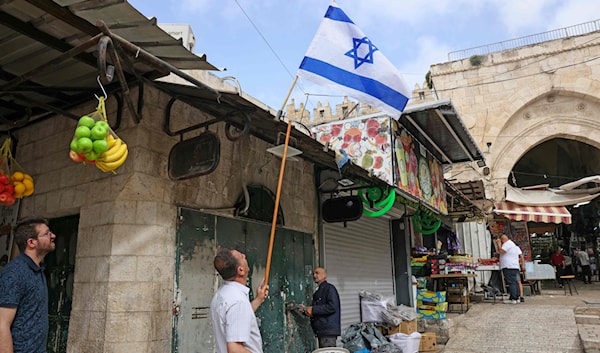 فلسطيني يزيل علماً للعدو  في القدس الشرقية وضعه المتطرفون أثناء إحيائهم ذكرى احتلال المدينة (أ ف ب)