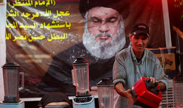 متطوّع يعد العصير لتوزيعه على مشاركين في مجالس عاشورائية في بغداد على خلفية ملصق للسيد الشهيد حسن نصرالله (أ ف ب)