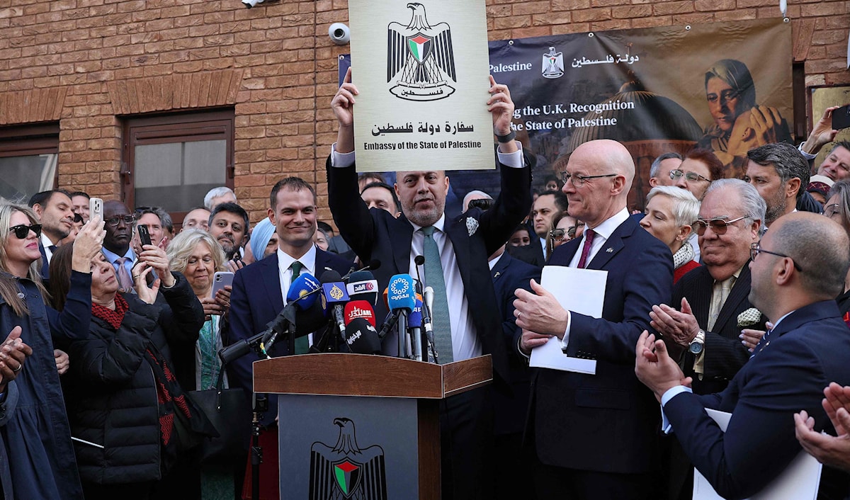 رئيس البعثة الدبلوماسية الفلسطينية حسام زملط يرفع لوحة كُتب عليها «سفارة دولة فلسطين» (أ ف ب)