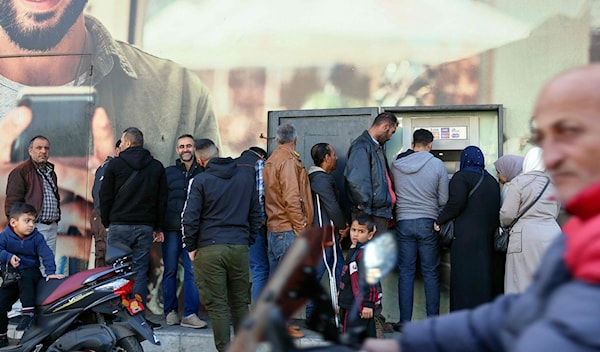 موظفون ينتظرون سحب أموالهم أمام صراف آلي (أ ف ب)