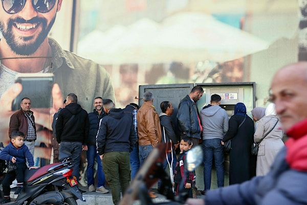 موظفون ينتظرون سحب أموالهم أمام صراف آلي (أ ف ب)