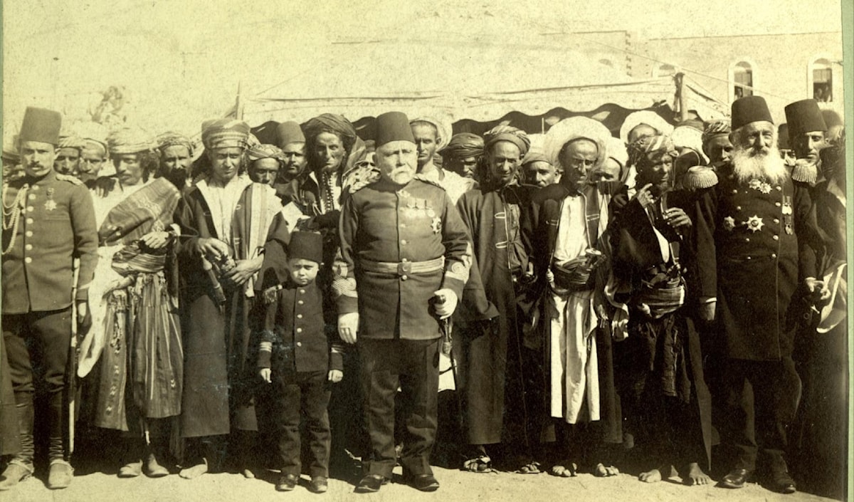 ضابط عثماني بالزّي العسكري إلى جانب عدد من اليمنيين بالملابس المحلية مطلع القرن العشرين (أرشيف)