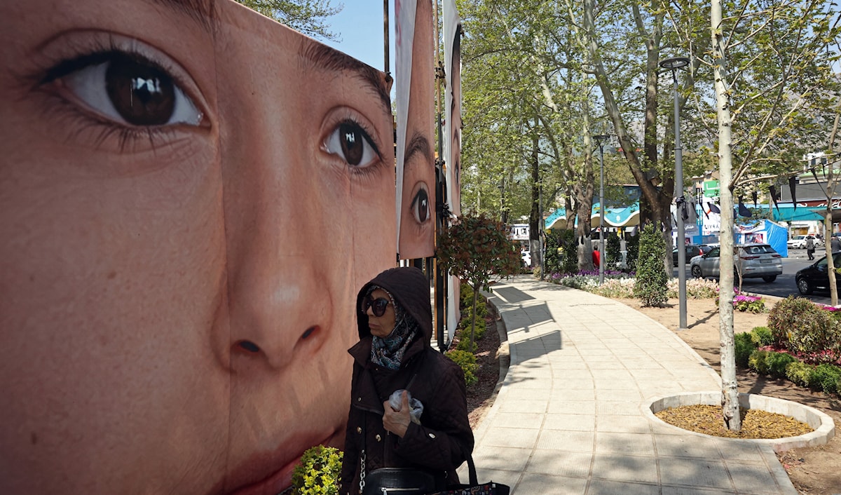 إيرانية في طهران تعبر قرب ملصق لإحدى ضحايا القصف الأميركي على مدرسة ميناب جنوب إيران (أ ف ب)