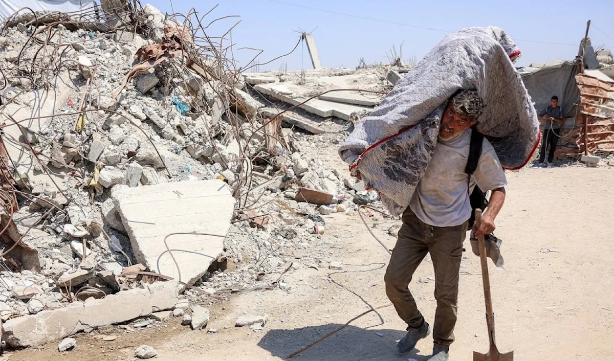 فلسطيني يحمل أمتعة على كتفه، بمحاذاة الأنقاض في مخيم للنازحين بغزة (أ ف ب)