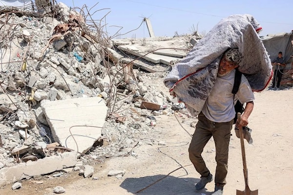 فلسطيني يحمل أمتعة على كتفه، بمحاذاة الأنقاض في مخيم للنازحين بغزة (أ ف ب)